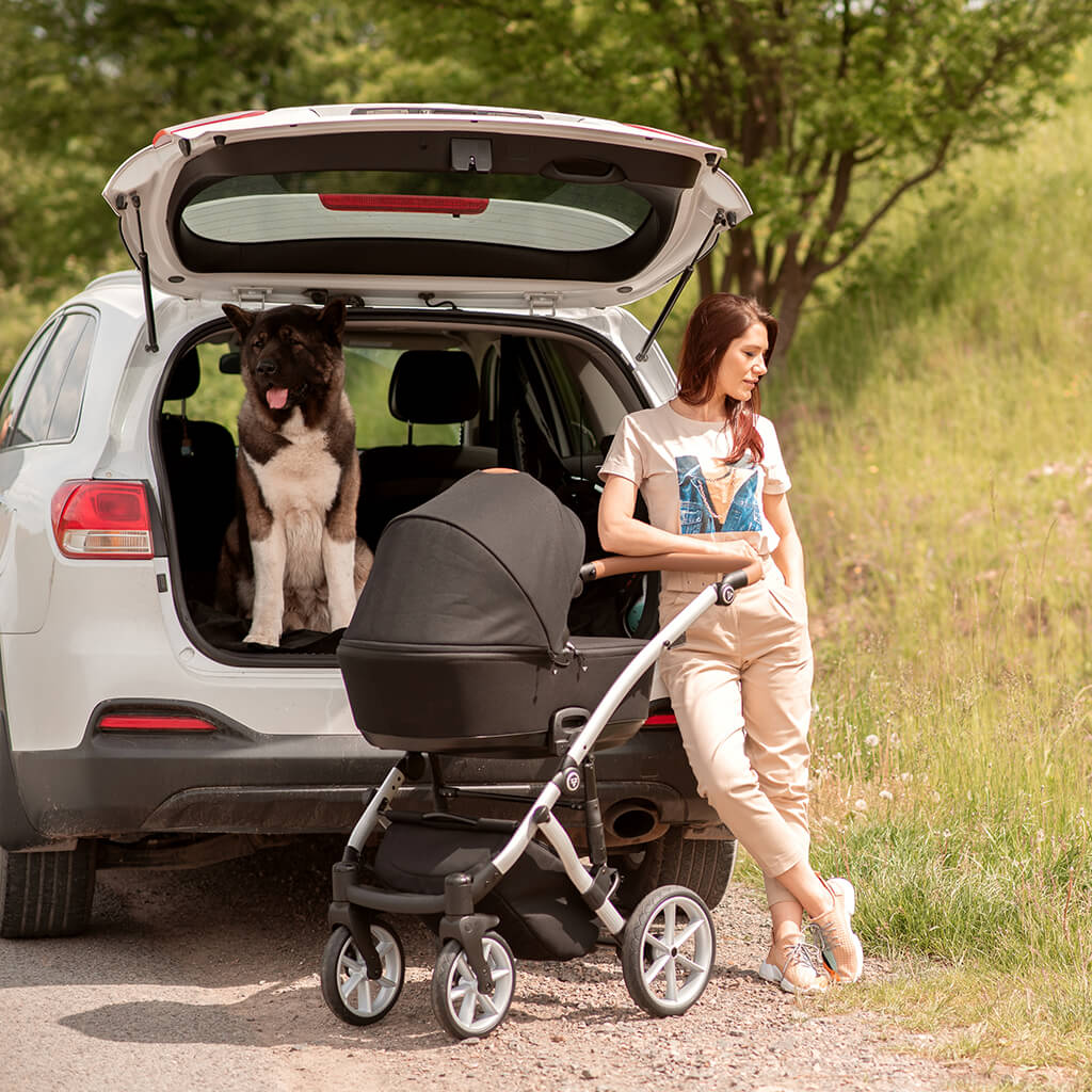 Frau mit Hund im Kofferraum und einem schwarzen Kinderwagen